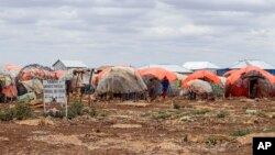 FILE - A woman walks past makeshift shelters at a camp for the internally displaced on the outskirts of Baidoa, in the South West State of Somalia, Oct. 12, 2022.