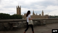 FILE - A pedestrian walks opposite The Palace of Westminster, the official name of Britain's Houses of Parliament, home to the House of Lords and the House of Commons, in London on July 21, 2022.