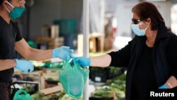 Un vendeur portant un masque protecteur livre un sac en plastique à un client d'un marché alimentaire en plein air qui a rouvert après le confinement dû au coronavirus à Cisternino, en Italie, le 27 avril 2020. REUTERS / Alessandro Garofalo - RC20DG9J93DO