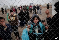 A child looks at a photographer as displaced people wait for aid at a camp east of Mosul, Iraq, Feb. 15, 2017.