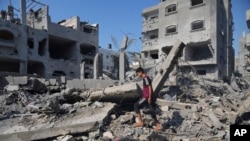 Warga Palestina berdiri di dekat bangunan yang hancur akibat serangan udara Israel di Deir al-Balah, selatan Jalur Gaza, Sabtu, 14 Oktober 2023. (AP /Hatem Moussa)