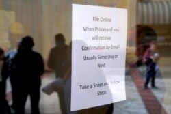 FILE - People who lost their jobs are reflected in the door of an Arkansas Workforce Center as they wait in line to file for unemployment following an outbreak of the coronavirus disease, in Fort Smith, Ark., April 6, 2020.