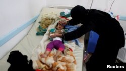 FILE - A woman helps her son as he lies on a bed at a cholera treatment center in Sanaa, Yemen, June 6, 2017.