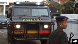 An armed police officer stands guard near an armored vehicle outside a local police office after a bomb went off in Cirebon, West Java, Indonesia, April 14, 2011