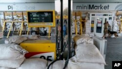 FILE - A gas station pump is fortified with sand bags as a Ukrainian serviceman exits a store in Kostiantynivka, Donetsk region, eastern Ukraine, Aug. 15, 2022. 