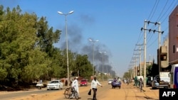 Des personnes déplacées par le conflit au Soudan marchent le long d'une route tandis que de la fumée s'élève au loin lors d'affrontements à Wad Madani, la capitale de l'État d'al-Jazirah, le 16 décembre 2023.