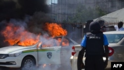 A Nigerian police officers watches a police vehicle as it goes up in flames following clashes with supporters of Islamic Movement of Nigeria (IMN) protesting against the imprisonment of their leader Ibrahim Zakzaky, in Abuja, on Oct. 30, 2018. 