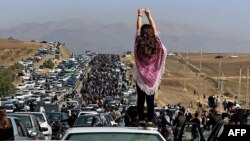 FILE - This UGC image posted on Twitter reportedly on Oct. 26, 2022 shows an unveiled woman standing atop a vehicle as thousands make their way towards a cemetery Mahsa Amini's hometown to mark 40 days since her death.