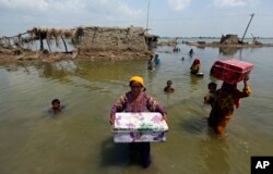 Women carry belongings from their flooded home after monsoon rains, in the Qambar Shahdadkot district of Sindh province, Pakistan, Sept. 6, 2022. Millions have lost their homes in flooding this year that many experts have blamed on climate change.