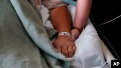 FILE - A woman, who is on oxygen as she recovers from COVID-19, holds the hand of her husband, who also contracted COVID-19, as he is kept alive with the help of an oxygenation machine at a medical center in Shreveport, La., Aug. 18, 2021.