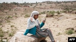 FILE - A woman attempts to get a mobile phone signal after most of an area was in blackout, in Samre, southwest of Mekele in Tigray region, Ethiopia, on June 20, 2021.