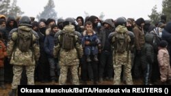 Belarusian service members stand guard as migrants gather for the distribution of humanitarian aid in a makeshift camp on the Belarusian-Polish border in the Grodno region on November 14, 2021. (Oksana Manchuk/BelTA/Handout via Reuters)