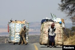 Steven Lesoona na Thabang Pule, wakusanya takataka, wakivuta matoroli yaliyosheheni takataka zinazopelekwa kuchakatuliwa wakikabiliana na uhaba wa ajira huko Naturena, karibu na Johannesburg, Afrika Kusini, Julai 3, 2023.