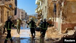Timu ya waokoaji kutoka jeshi la Misri wakibeba miili wakipita katikati ya majengo yaliyoharibiwa na kimbunga na mvua kubwa zilizoikumba Libya, huko Derna, Sept. 13, 2023.