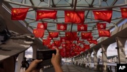 FILE - Chinese tourists take photos of Chinese and Hong Kong flags marking the 26th anniversary of the city's handover from Britain to China in Hong Kong, on June 27, 2023.