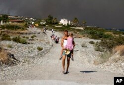 Čovek nosi dete dok napušta oblast šumskih požara, na ostrvu Rodos, Grčka, 22. jula 2023.