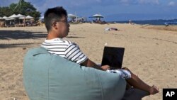 Армонио Лианг од Кина седи на плажа додека работи на својот компјутер во Бали, Индонезија, на 22 јуни 2023 година