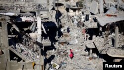 Anak-anak Palestina berjalan di antara rumah-rumah yang hancur akibat serangan Israel di tengah gencatan senjata sementara antara Israel dan Hamas, di kamp pengungsi Khan Younis, di selatan Jalur Gaza, 29 November 2023. (Foto: REUTERS/Mohammed Salem)