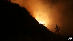 FILE - A volunteer uses a water hose to fight a wildfire near houses on the outskirts of Obidos, Portugal, early on Oct. 16, 2017.