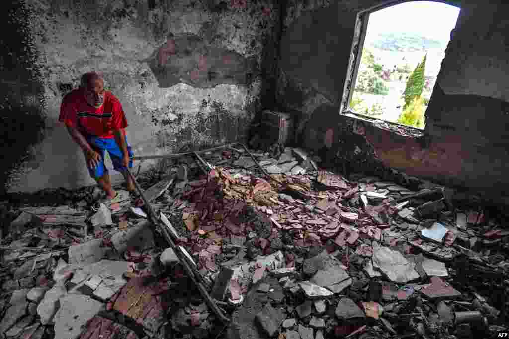 A man picks up a damaged metal frame while going through the rubble of a destroyed building in the aftermath of a forest fire near the town of Melloula in northwestern Tunisia close to the border with Algeria, July 26, 2023.
