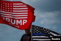 Seorang pendukung mantan Presiden AS Donald Trump memegang bendera pro-penegakan hukum sehari setelah dia didakwa oleh dewan juri Manhattan menyusul penyelidikan atas uang tutup mulut yang dibayarkan kepada bintang porno Stormy Daniels, di Palm Beach, Florida. (Foto: Reuters)