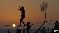 A man is silhouetted against the setting sun as he balances on a wire at a beach in the Israeli coastal city of Tel Aviv, Israel, on April 19, 2024.