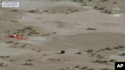 This image taken from video provided by NASA TV shows the capsule released by the Osiris-Rex spacecraft lying on the surface near the parachute after landing to Earth, Sept. 24 2023. (NASA TV via AP)