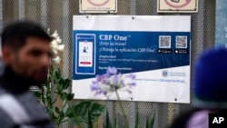 People waiting to apply for asylum stand in front or a sign for the CBP One app as they camp near the pedestrian entrance to the San Isidro Port of Entry, linking Tijuana, Mexico with San Diego, June 1, 2023, in Tijuana, Mexico. 