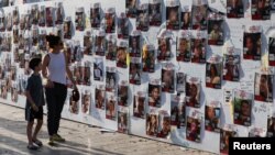 Жена и дете шетаат поминуваат покрај ѕид со слики од заложници во Газа откако беа киднапирани од страна на вооружени напаѓачи на Хамас на 7 октомври, 2023 година
