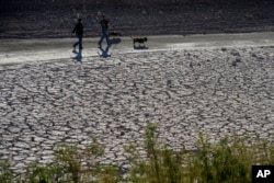 FILE - People walk by cracked earth in an area once under the water of Lake Mead at the Lake Mead National Recreation Area, Jan. 27, 2023, near Boulder City, Nevada.