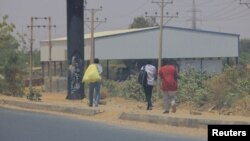 People cross the Halfaya Bridge as smoke rises in the background during clashes between the Sudanese army and paramilitary forces, as seen from Khartoum North, Sudan, April 15, 2023. 