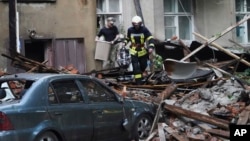 A firefighter helps a man carry belongings out of an apartment building damaged by a Russian attack in Sumy, Ukraine, July 3, 2023.