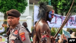 Seorang pemuda Papua (kanan) dalam pakaian tradisional, yang wajahnya dicat dengan warna Bendera Bintang Kejora yang dilarang pemerintah, saat demonstrasi menuntut referendum kemerdekaan provinsi Papua di Yogyakarta, 1 Desember 2023. (Foto: DEVI RAHMAN/AFP)