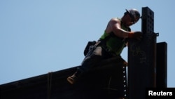 FILE - A worker installs steel beams on high-rise building under construction during a summer heat wave in Boston, June 30, 2021. 