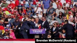 美国共和党总统候选人、美国前总统唐纳德·特朗普(Donald Trump)在宾夕法尼亚州巴特勒的竞选集会上被枪手击中右耳，随后美国特勤局人员将他搀扶起来。（2024年7月13日）