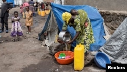 FILE - A displaced Congolese woman washes dishes in front of her tent at a camp for internally displaced people during the registration of civilians by the electoral commission as voters, in Kanyaruchinya near Goma, North Kivu province of the Democratic Republic of Congo Feb. 16, 2023.