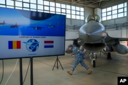 A Romanian serviceman walks under a Royal Netherlands Air Force F-16 in a hangar at the Baza 86 military air base, outside Fetesti, Romania, Nov. 13, 2023.