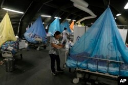 FILE - A doctor writes a prescription as patients suffering from dengue lie in beds in provisional tents at the Health Ministry in Piura, Peru, June 3, 2023.
