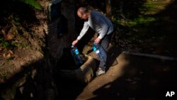 Joan Torrent fills plastic jugs at a natural spring in Gualba, about 50 kilometers, (31 miles) northwest of Barcelona, Spain, Jan. 31, 2024. Almost every day, he into the woods in search of drinking water. 