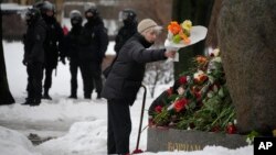 یک زن در شهر سنت پیترسبرگ در حضور پولیس در محل یادبود نوالنی گل می‌گذارد
