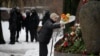 Police officers stand guard as a woman lays flowers for Alexey Navalny at the monument, a large boulder from the Solovetsky islands, where the first camp of the Gulag political prison system was established, in St. Petersburg, Russia, Feb. 17, 2024.