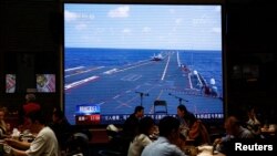 Customers dine near a giant screen broadcasting news footage of an aircraft taking off from China's Shandong aircraft carrier while taking part in a combat readiness patrol and "Joint Sword" exercises around Taiwan, at a restaurant in Beijing, China April 10, 2023. 