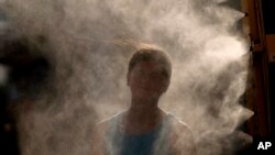 A woman cools off in a mister at Kauffman Stadium as temperatures approach 100 degrees fahrenheit before a baseball game between the Kansas City Royals and the Cleveland Guardians, June 28, 2023, in Kansas City, Mo.