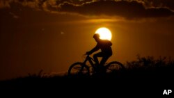 FILE - A cyclist tops a hill on a hot day at sunset, Aug. 20, 2023, in San Antonio. The U.N. weather agency said Earth sweltered through the hottest summer ever as record heat in August capped a brutal three months in the Northern Hemisphere.