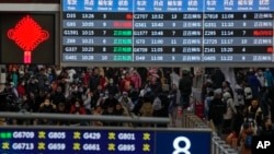Travelers with luggage walk beneath a trains departure board as they arrive at the West Railway Station to catch their trains, in Beijing, Feb. 7, 2024. 