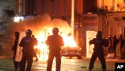 A car burns as Irish policemen stand at the scene of an attack in Dublin, Nov. 23, 2023. 