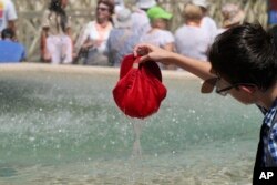 A child plunges his hat into a fountain in St. Peter's Square at Vatican City, July 16, 2023, as southern Europe experiences a heatwave.