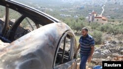 资料照片：2023年12月3日，一名巴勒斯坦男子在以色列占领的约旦河西岸萨尔菲特附近检查一辆在以色列定居者突袭中被烧毁的汽车。（路透社照片）