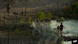FILE - A Texas trooper talks with migrants as they walk along concertina wire and try to cross the Rio Grande at the Texas-U.S. border in Eagle Pass, Texas, July 6, 2023.