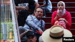 A woman cools herself off with a fan while sitting down in the Time Square area of New York City, June 18, 2024.